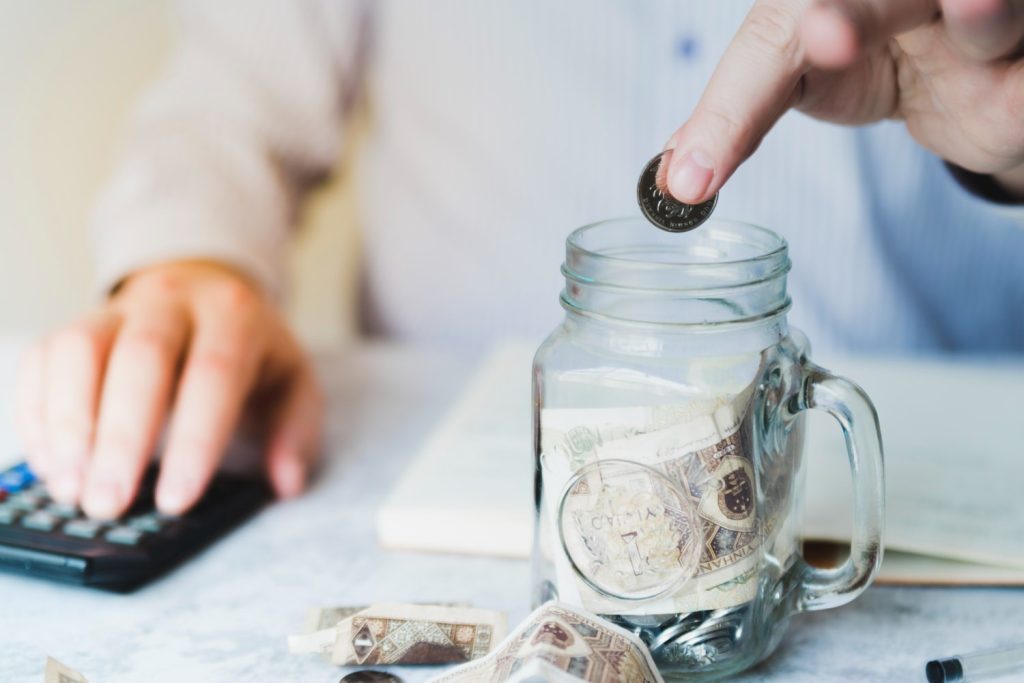 Business professional calculating cost savings from cloud based phone systems while putting coins into a savings jar next to a calculator