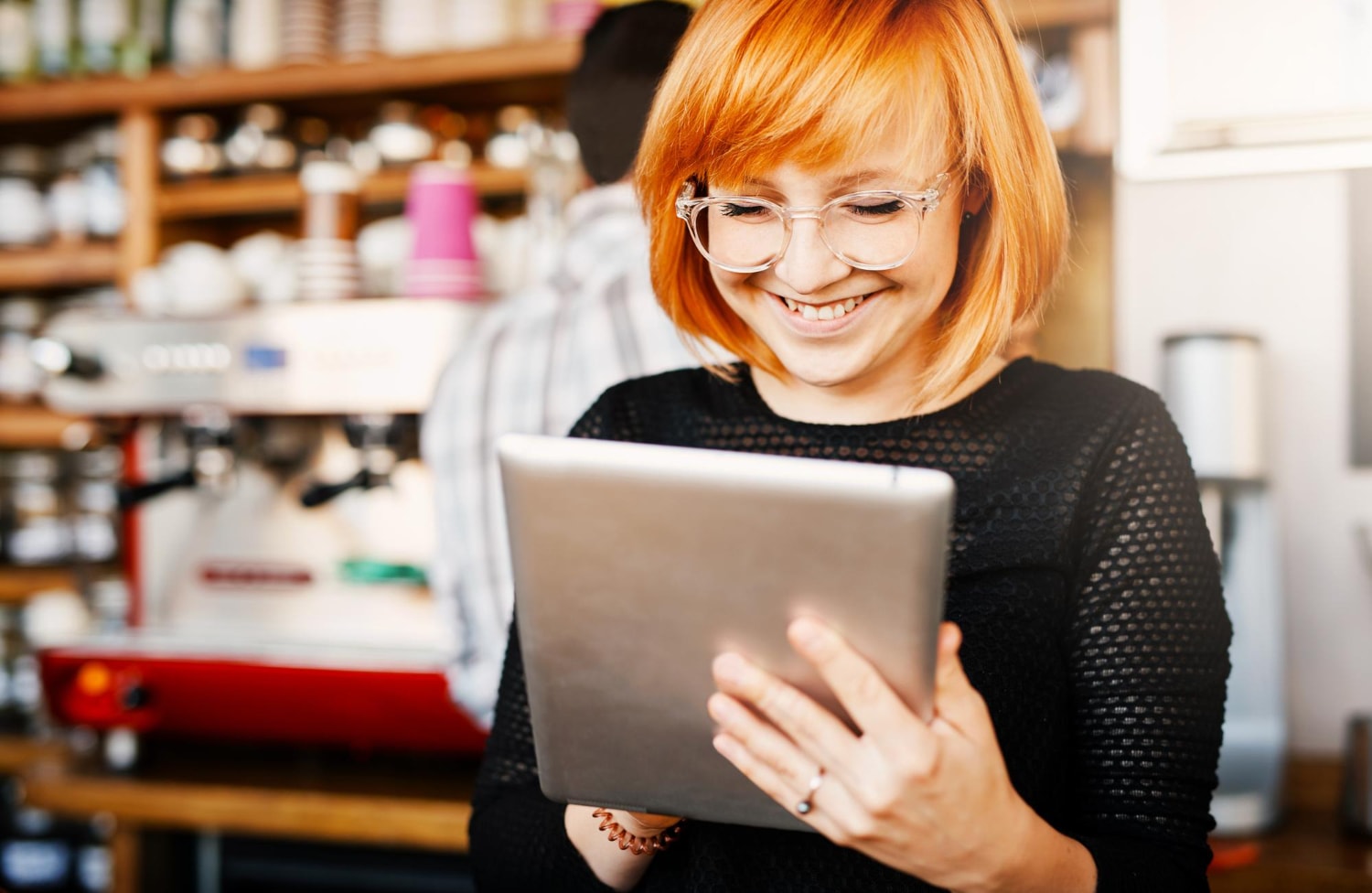 A smiling woman with red hair uses a tablet in a cozy café, reflecting the flexibility of business internet and the role of fast, reliable internet solutions in supporting entrepreneurs and digital professionals.